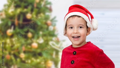 Shot of an adorable child dressed in a Christmas outfit and looking at camera with a tree in the background at home