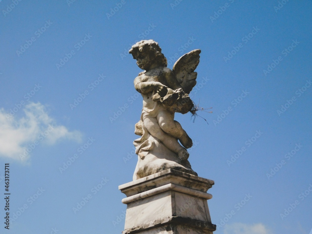 Statue of a little stone angel with blue sky in the background. 
