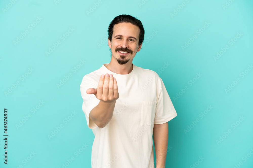 Young caucasian man isolated on blue background inviting to come with hand. Happy that you came Young caucasian man isolated on blue background inviting to come with hand. Happy that you came