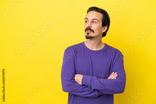Young caucasian man isolated on yellow background looking to the side