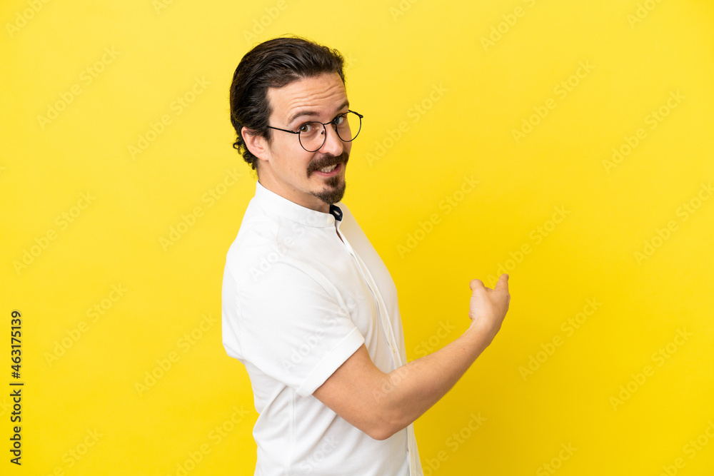 Young caucasian man isolated on yellow background pointing back Young caucasian man isolated on yellow background pointing back