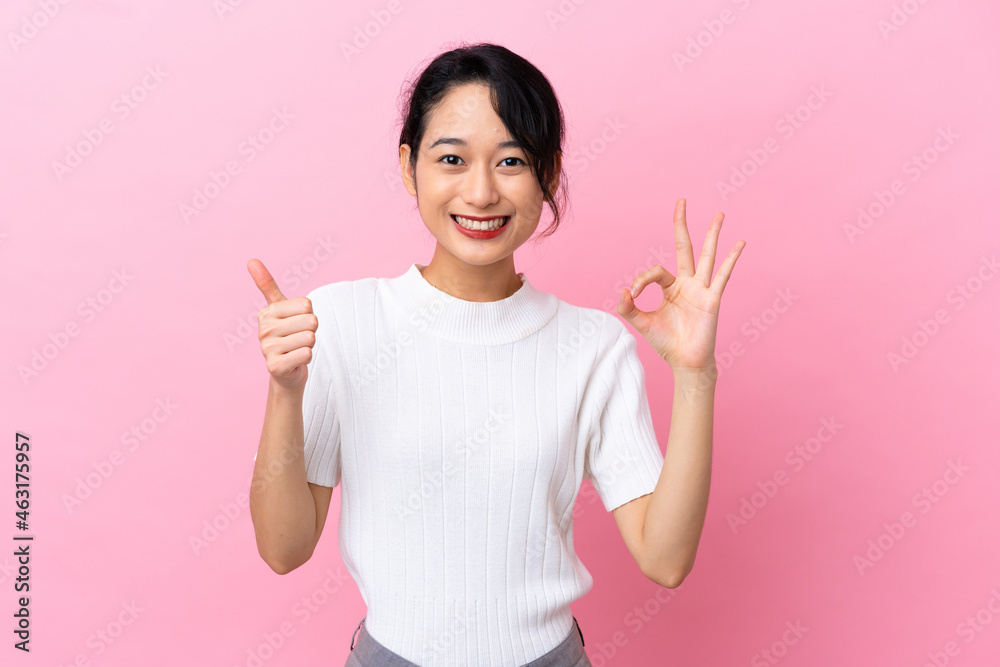 Young Vietnamese woman isolated on pink background showing ok sign and thumb up gesture Young Vietnamese woman isolated on pink background showing ok sign and thumb up gesture