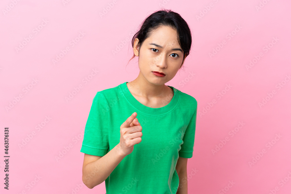Young Vietnamese woman isolated on pink background frustrated and pointing to the front Young Vietnamese woman isolated on pink background frustrated and pointing to the front
