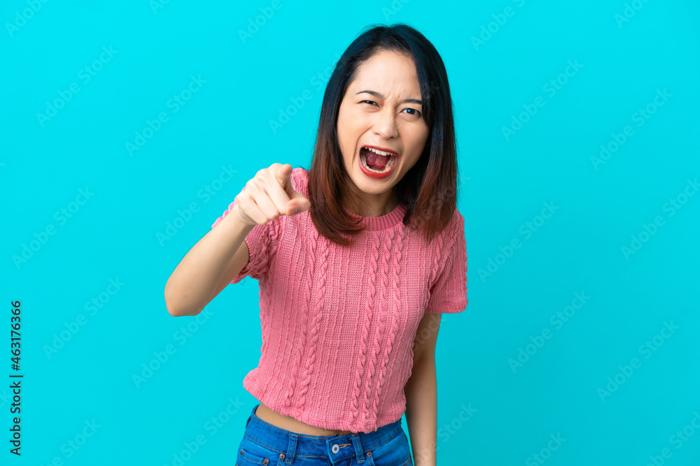 Young Vietnamese woman isolated on blue background frustrated and pointing to the front Young Vietnamese woman isolated on blue background frustrated and pointing to the front
