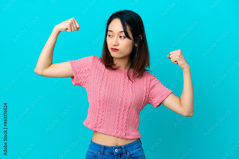 Young Vietnamese woman isolated on blue background doing strong gesture Young Vietnamese woman isolated on blue background doing strong gesture