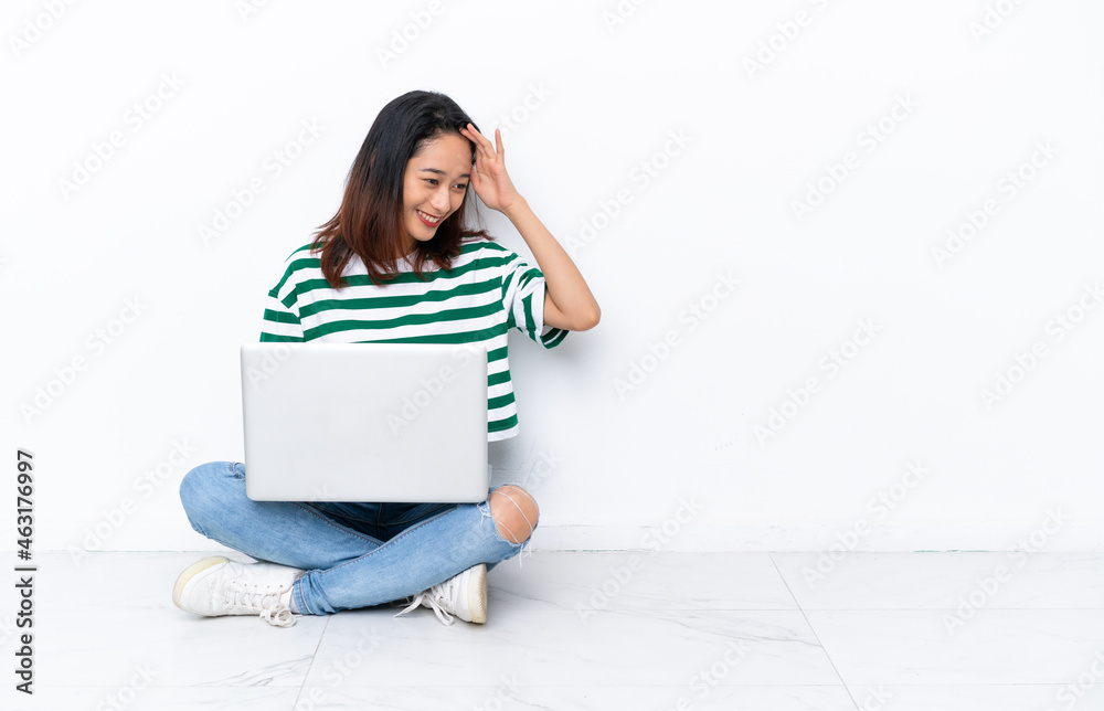 Young Vietnamese woman with a laptop sitting on the floor isolated on white wall laughing Young Vietnamese woman with a laptop sitting on the floor isolated on white wall laughing