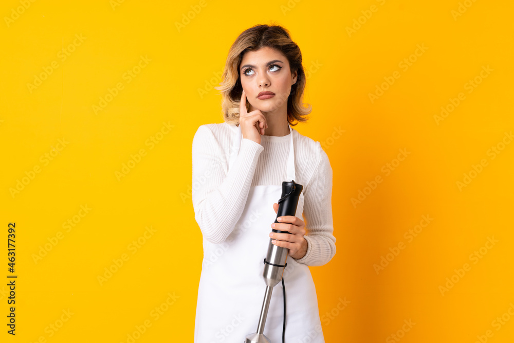 Girl using hand blender isolated on yellow background thinking an idea