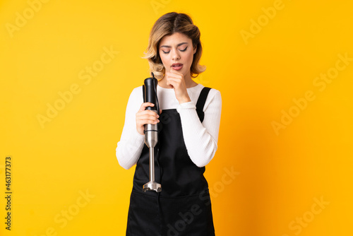 Girl using hand blender isolated on yellow background coughing a lot