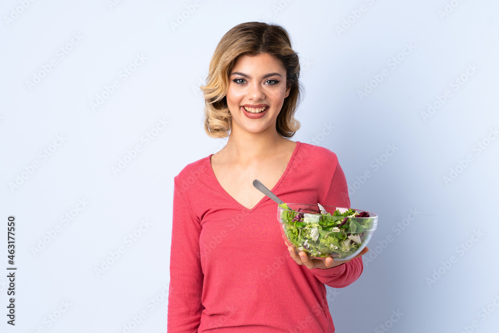 Teenager woman with salad isolated on blue background smiling a lot Teenager woman with salad isolated on blue background smiling a lot
