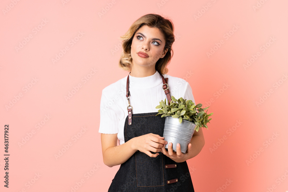 Russian gardener girl holding a plant isolated on pink background thinking an idea Russian gardener girl holding a plant isolated on pink background thinking an idea