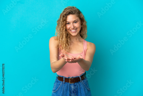 Young blonde woman isolated on blue background holding copyspace imaginary on the palm to insert an ad