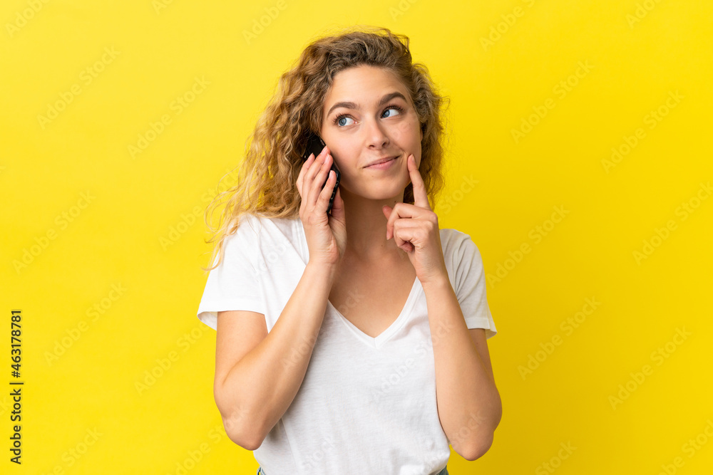 Young blonde woman using mobile phone isolated on yellow background thinking an idea while looking up Young blonde woman using mobile phone isolated on yellow background thinking an idea while looking up