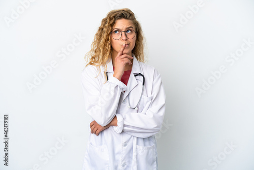 Young doctor blonde woman isolated on white background having doubts while looking up