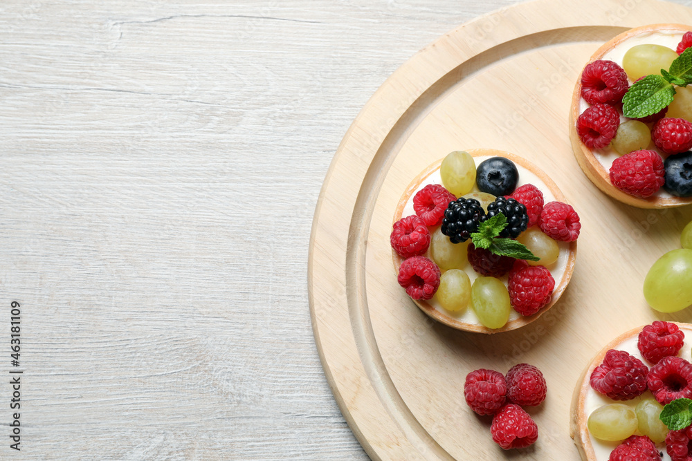 Delicious tartlets with berries on light wooden table, top view. Space for text Delicious tartlets with berries on light wooden table, top view. Space for text