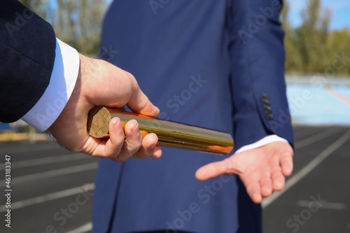 Businessman passing baton to his partner outdoors, closeup