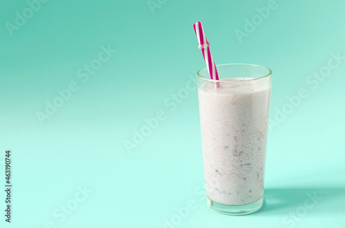 Milkshake in a transparent container with pieces of natural berries and a red tube of kopi space. Cocktail of ice cream, milk and berries on a colored background