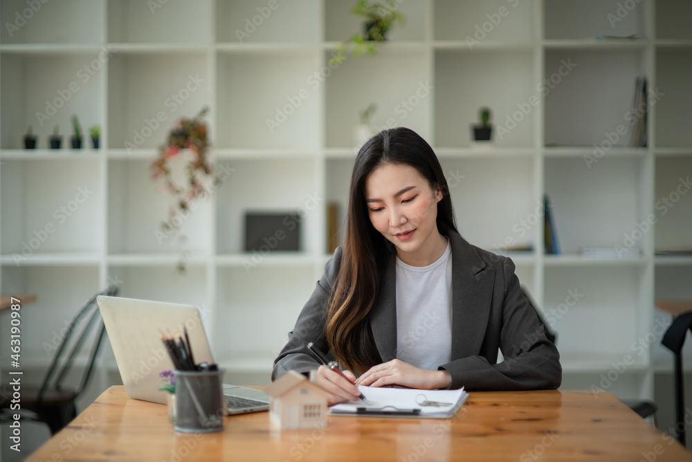 Businesswoman writing a note while using laptop at a table in an office.