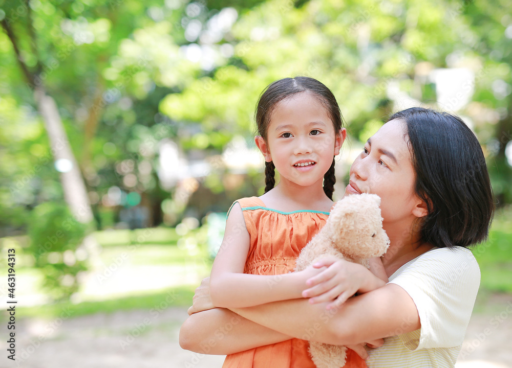 Portrait of Asian mother cuddle daughter and hugging teddy bear doll in the garden. Mom and child girl with love and relationship concept. Portrait of Asian mother cuddle daughter and hugging teddy bear doll in the garden. Mom and child girl with love and relationship concept.