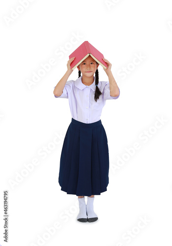 Asian little schoolgirl in Thai school uniform standing with hold open book cover over head isolated on white background. Full length with Clipping path