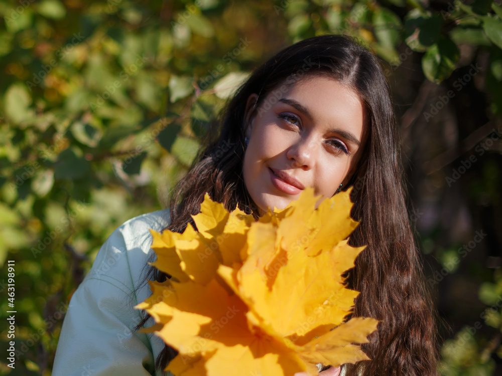 A happy young woman in an autumn park with a bunch of maple leaves in hands