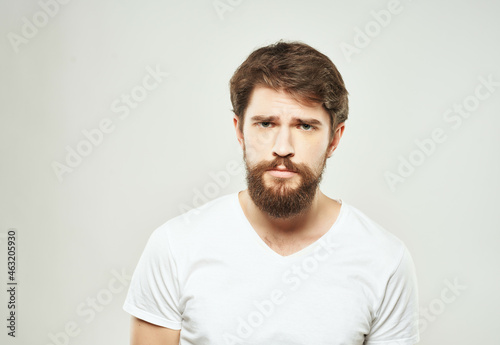 bearded man in a white t-shirt irritated facial expression light background