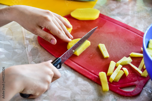 A child in the kitchen cuts potatoes on the board. Cooking fried potatoes at home