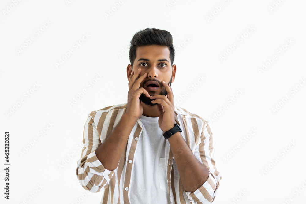 Oh no. Shocked young Indian man holding hands behind head and keeping mouth open while standing against white background Oh no. Shocked young Indian man holding hands behind head and keeping mouth open while standing against white background