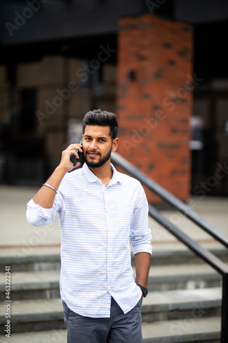 Handsome indian man with laptop talking on phone walking on the stairs in city