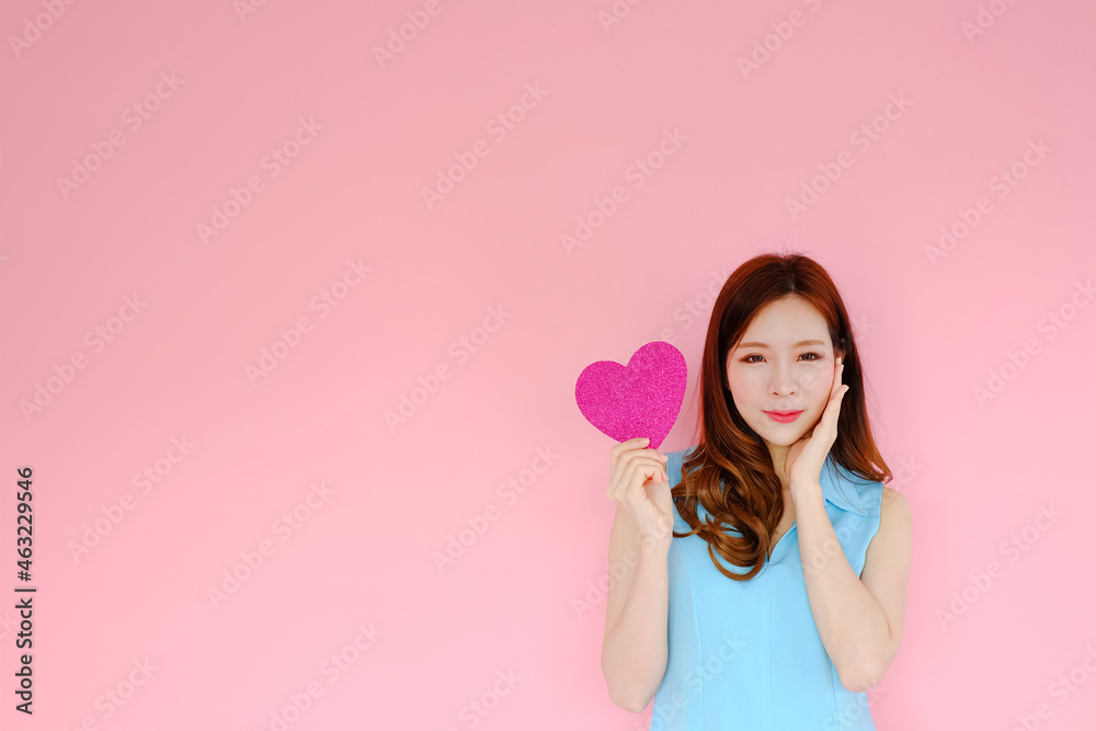 Portrait beautiful asian woman on pink background, valentine day in love concept, model holding red heart sign in hand Portrait beautiful asian woman on pink background, valentine day in love concept, model holding red heart sign in hand