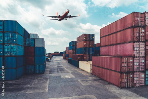 Cargo container for overseas shipping in shipyard with airplane in the sky . Logistics supply chain management and international goods export concept .