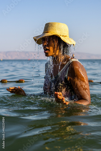 black woman bathing in sea of galilee srael. water dripping and splashing as she enjoys lake tiberius and sun. shot on fast shutter speed to freeze the water. photo