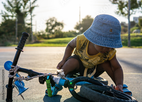 black interracial mixed ethnicty leanning to fix bicycle in park. hat on. sunset in Ravid Israel.