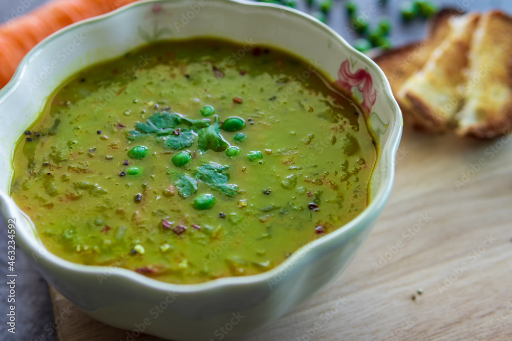 Homemade pea soup served with toasted bread or croutons. Green split pea soup rich in flavors, vegetables, herbs and healthy ingredients. Tasty soup for winter in a decorative bowl on a wooden board. Homemade pea soup served with toasted bread or croutons. Green split pea soup rich in flavors, vegetables, herbs and healthy ingredients. Tasty soup for winter in a decorative bowl on a wooden board.