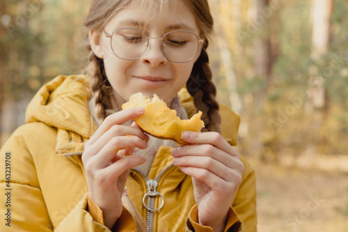 Closeup girl in glasses and yellow jacket eat pumpkin. Outdoor picnic. Little helper in preparation for Halloween