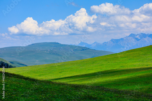 Green grass and mountain with blue sky background.Green grassland landscape in Xinjiang,China.