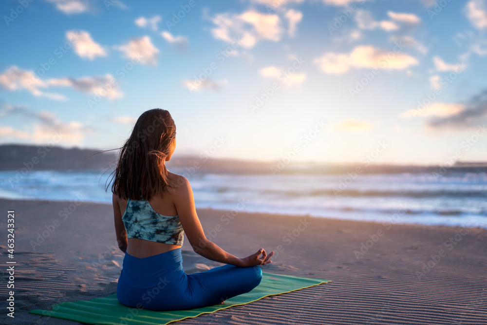 latin woman meditating or doing yoga at sunset on the beach