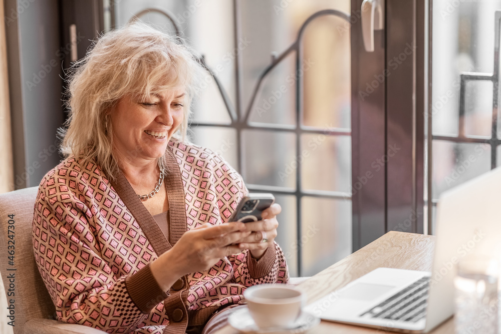 Mobile phone in the hands of an attractive adult blonde woman sitting at a table in a cafe Mobile phone in the hands of an attractive adult blonde woman sitting at a table in a cafe