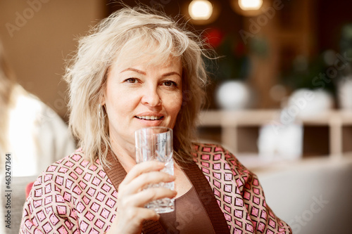 Portrait of an attractive adult smiling blonde of European appearance with a glass of water in her hands close-up
