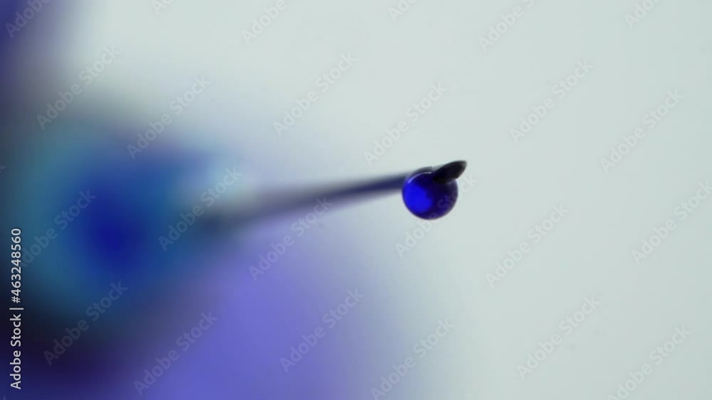 Drop Of Blue Liquid On Needle Tip From Syringe. Drop Falling in Slow Motion, Macro Shooting Drop Of Blue Liquid On Needle Tip From Syringe. Drop Falling in Slow Motion, Macro Shooting