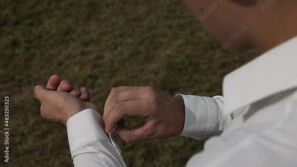 A young man puts on a white shirt in the street. The groom puts on a suit on the street and fastens the buttons. A businessman buttons up his shirt sleeves in the street. Young man in the garden. A young man puts on a white shirt in the street. The groom puts on a suit on the street and fastens the buttons. A businessman buttons up his shirt sleeves in the street. Young man in the garden.