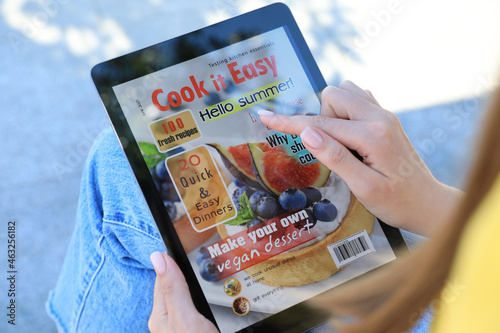 Woman reading online magazine on tablet outdoors, closeup photo