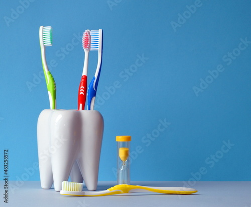 Toothbrushes are in a glass, there is an hourglass next to it, to count the time of brushing your teeth, and one brush lies on the table