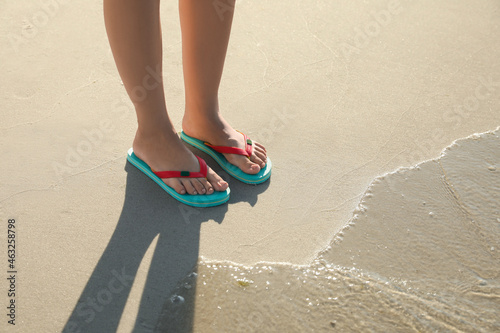 Woman wearing flip flops on sandy beach, closeup