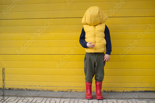 Little boy hides his face with his coat hood
