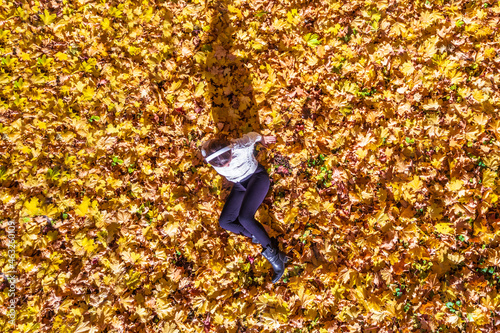 Top view. Beautiful happy young woman lying and relaxing on the autumn maple leaves in the park. Aerial  drone view