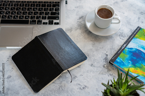 there is a laptop on the table, a mug of coffee and a notebook next to it