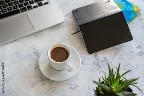 there is a laptop on the table, a mug of coffee and a notebook next to it