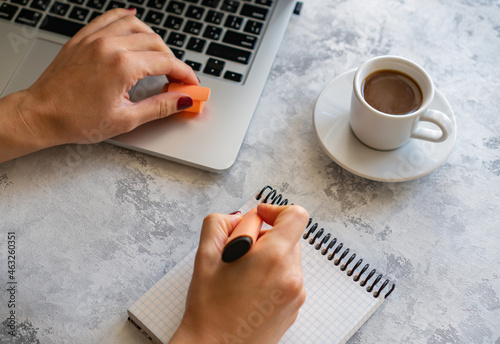 the girl makes notes in a notebook, there is a computer and a mug of coffee nearby