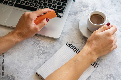 the girl makes notes in a notebook, there is a computer and a mug of coffee nearby