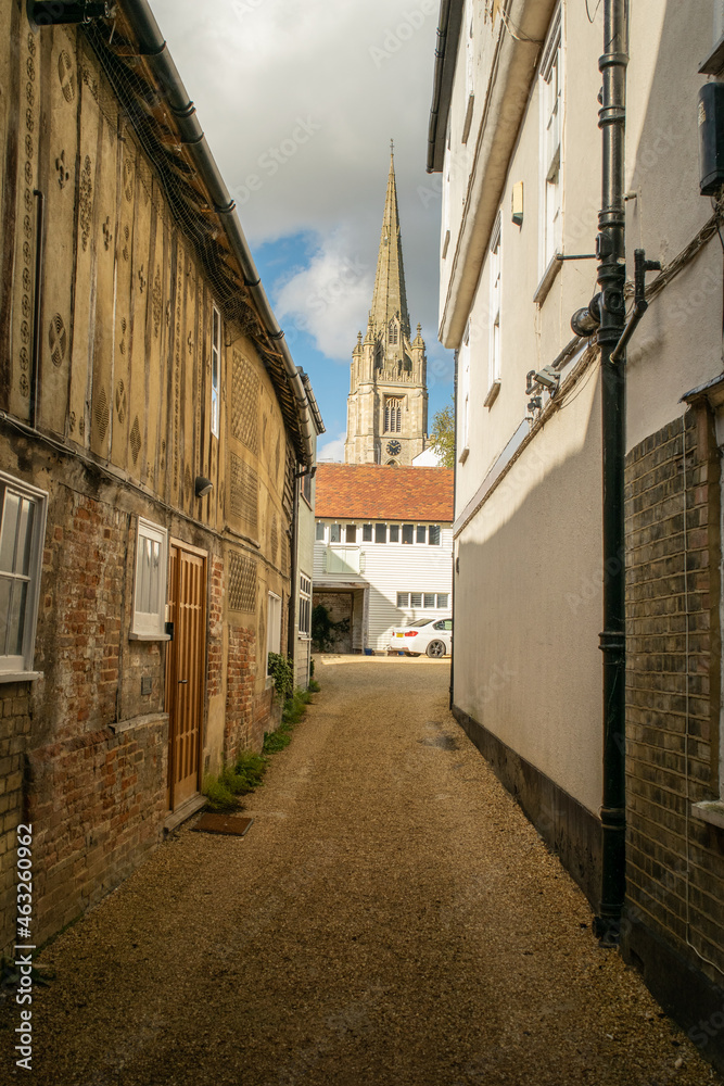 Facade of old brick terraces houses at an alley with a cathedral tower visible at Saffron Walden, England